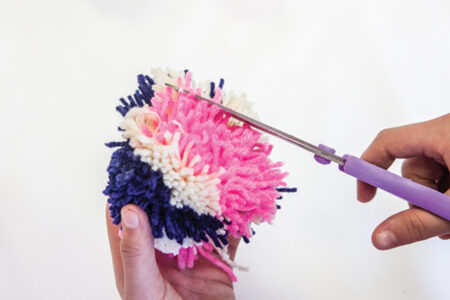 person trimming yarn pom pom with scissors